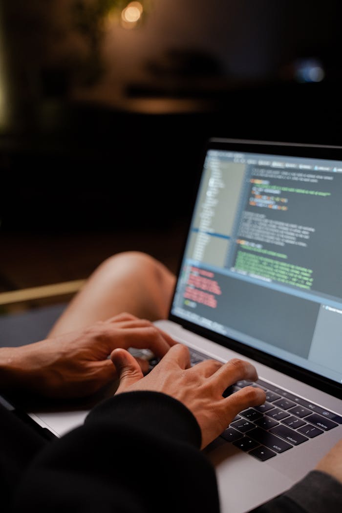 A programmer typing code on a laptop in a dimly lit room, reflecting the tech-driven work environment.